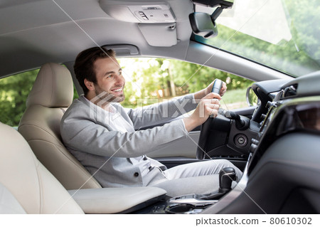 Side view of confident, handsome young businessman in formal wear driving his car, road to office 80610302
