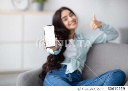 Awesome mobile app. Indian lady presenting smartphone with white blank screen and showing thumb up at home, mockup Awesome mobile app. Indian lady presenting smartphone with white blank screen and showing thumb up at home, mockup 80610359