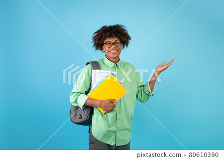 Excited african american student guy showing empty space and smiling, posing over blue background, copy space 80610390