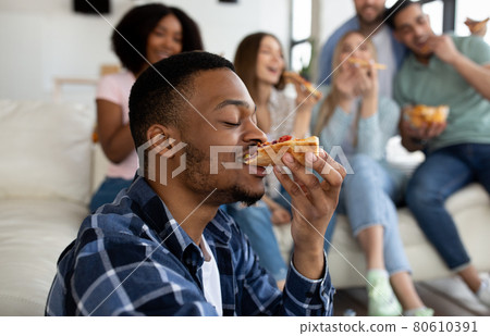 Funky black guy eating tasty pizza with his multinational friends, enjoying social gathering at home 80610391