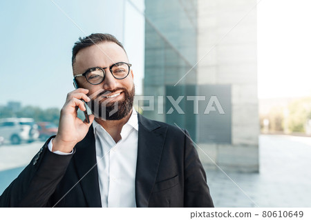 Happy CEO or manager talking on mobile phone and smiling while walking near office center during break, empty space 80610649