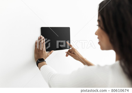 Young black lady controlling house with digital touch screen panel installed on white wall in the living room, mockup Young black lady controlling house with digital touch screen panel installed on white wall in the living room, mockup 80610674