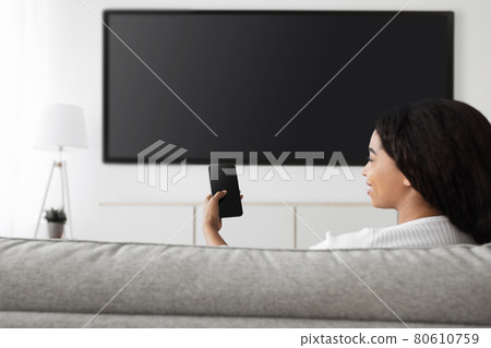 Smart home. Excited african american woman with cellphone connected to TV, plasma television with empty screen, mockup Smart home. Excited african american woman with cellphone connected to TV, plasma television with empty screen, mockup 80610759