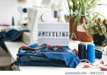 Denim Upcycling Ideas, Using Old Jeans, Repurposing Jeans, Reusing Old Jeans, Upcycle Stuff. Lightbox with text Upcycling, Stack of old blue jeans, scissors, thread and sewing tools in sewing studio. Denim Upcycling Ideas, Using Old Jeans, Repurposing Jeans, Reusing Old Jeans, Upcycle Stuff. Lightbox with text Upcycling, Stack of old blue jeans, scissors, thread and sewing tools in sewing studio. 80611517
