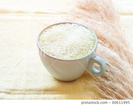 Matcha tea latte morning antioxidant hot drink in blue cup on yellow table cloth with pampas grass Matcha tea latte morning antioxidant hot drink in blue cup on yellow table cloth with pampas grass 80611995
