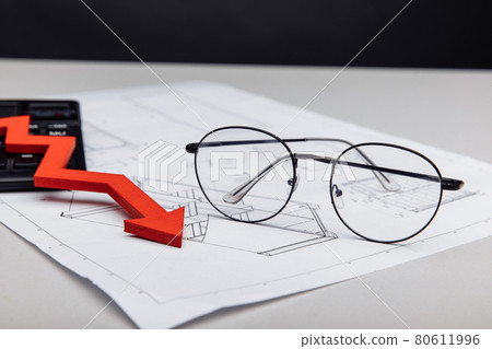 Financial and investment concept. Glasses and arrow down on architectural project close-up Financial and investment concept. Glasses and arrow down on architectural project close-up 80611996