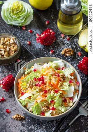 Autumn dietary Chinese cabbage salad fresh vegetable, carrots, apple, nuts and pomegranate with vinaigrette dressing on a dark stone table. Autumn dietary Chinese cabbage salad fresh vegetable, carrots, apple, nuts and pomegranate with vinaigrette dressing on a dark stone table. 80612438