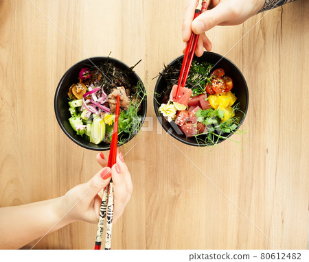 Man and woman eating poke salad with chopsticks. Dab tuna salad in a bowl. People in the restaurant 80612482