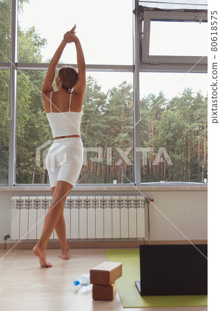 Sports woman stretches while standing at the window. Back view 80618575