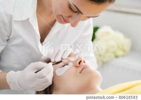 Cosmetician applying eyelash treatment to woman customer Cosmetician applying eyelash treatment to woman customer 80618583