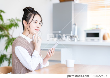 一個年輕的女人，在客廳裡操作智能手機 80622404