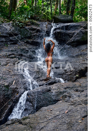 Beautiful woman posing at small tropical waterfall Beautiful woman posing at small tropical waterfall 80622473