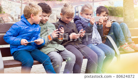 Kids playing with smartphones on bench Kids playing with smartphones on bench 80624872