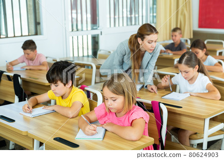 Focused preteen pupils studying in classroom with female teacher Focused preteen pupils studying in classroom with female teacher 80624903