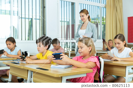 Absorbed preteen school children using mobile phones at lesson 80625113