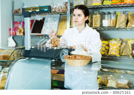 Young saleswoman is weighing cookies Young saleswoman is weighing cookies 80625161