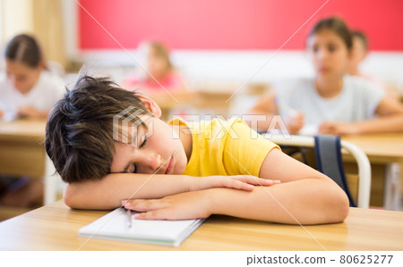 Bored tween boy sleeping at desk in classroom during lesson Bored tween boy sleeping at desk in classroom during lesson 80625277
