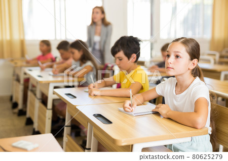 Diligent tween schoolgirl making notes of teacher lecture 80625279