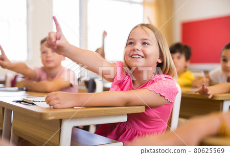 Girl raising hand to answer during lesson at classroom Girl raising hand to answer during lesson at classroom 80625569