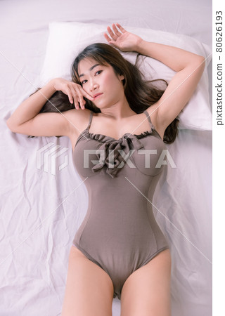 Sexy Asian woman in brown pajamas on a white bed - Stock Photo