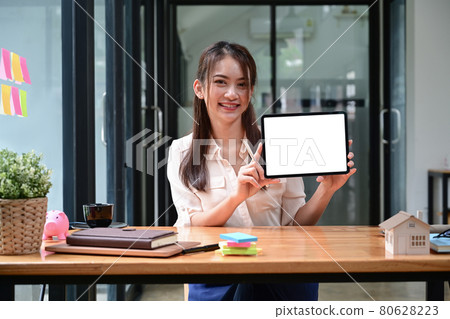 Cheerful young female holding and showing digital tablet with empty display. 80628223