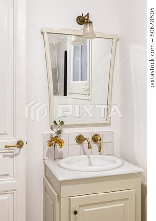 Bathroom decorated in beige color with small sink, bronze faucet and vintage mirror. Interior of retro or classic style. 80628505