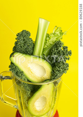 Smoothie recipe. Green smoothie of vegetables avocado, celery, cale salad, spinach in a blender on a yellow background. Vegan and healthy food detox concept Smoothie recipe. Green smoothie of vegetables avocado, celery, cale salad, spinach in a blender on a yellow background. Vegan and healthy food detox concept 80629188