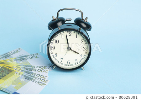 Time and money concept. Euro cash and alarm clock on a blue background Time and money concept. Euro cash and alarm clock on a blue background 80629391