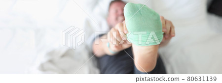 Man lying on bed and putting on green sock closeup Man lying on bed and putting on green sock closeup 80631139