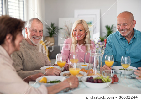 Group of senior friends having party indoors, talking when eating at the table. 80632244
