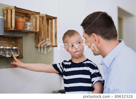 Father with happy down syndrome son indoors in kitchen, cooking. 80632328