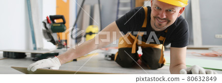 Man builder in yellow helmet lying laminate boards on floor Man builder in yellow helmet lying laminate boards on floor 80632849