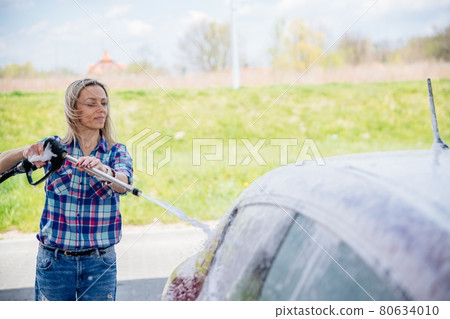 Woman at the self-service car wash station washing the foam off her car. Woman at the self-service car wash station washing the foam off her car. 80634010