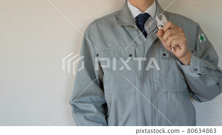 A man wearing work clothes with a safety mark and holding a tool. 80634863