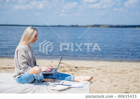 Blonde woman with a laptop sending messages while working remotely on vacation. 80635433