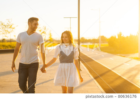 Portrait of young couple in love holding hands walking in city park in sunny summer day on background of bright sunlight. 80636176