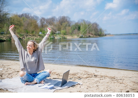 Excited woman, female freelancer with laptop keeping arms raised while working remotely during summer vacation. 80638053