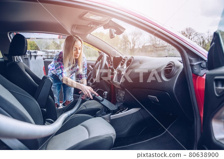Woman removs dust with a vacuum cleaner during car cleaning. 80638900