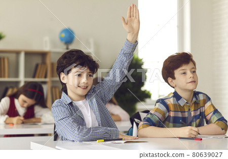 Schoolboy sits in a classroom with his hand raised wanting to give the right answer or participate. Schoolboy sits in a classroom with his hand raised wanting to give the right answer or participate. 80639027