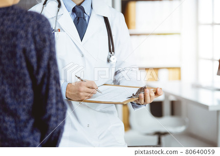 Female doctor and male patient discussing current health examination while sitting in sunny clinic, close-up Female doctor and male patient discussing current health examination while sitting in sunny clinic, close-up 80640059