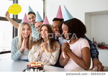 Young international friends congratulating Caucasian lady with birthday, presenting festive cake, making wish at home Young international friends congratulating Caucasian lady with birthday, presenting festive cake, making wish at home 80640284