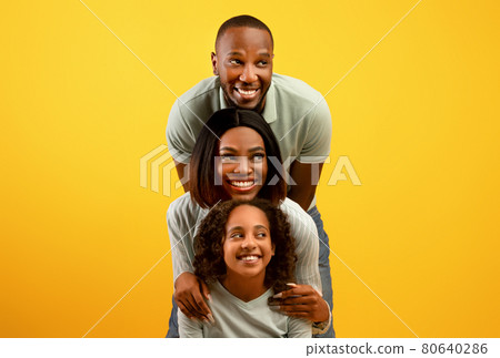 Promo concept. Happy black family of three looking aside at free copy space on yellow studio background Promo concept. Happy black family of three looking aside at free copy space on yellow studio background 80640286