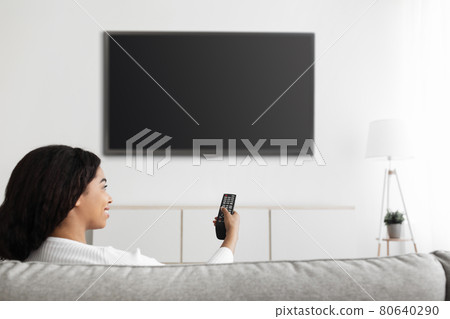 Fun in the evening. Relaxed black lady watching TV pointing remote control at flatscreen television with black screen Fun in the evening. Relaxed black lady watching TV pointing remote control at flatscreen television with black screen 80640290