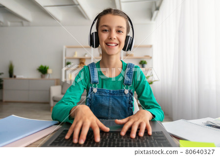 Girl sitting at desk, using laptop, wearing headset, typing Girl sitting at desk, using laptop, wearing headset, typing 80640327