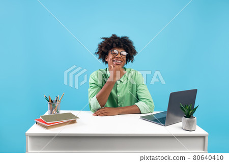 Online school or educational course concept. Excited smiling black guy sitting at desk and using laptop, blue background Online school or educational course concept. Excited smiling black guy sitting at desk and using laptop, blue background 80640410