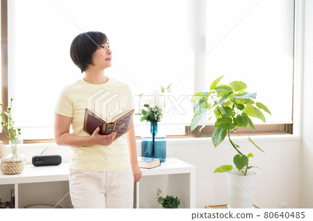 A woman standing by the window and reading a book 80640485