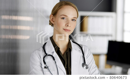 Friendly smiling female doctor standing in clinic. Portrait of friendly physician woman. Perfect medical service in hospital Friendly smiling female doctor standing in clinic. Portrait of friendly physician woman. Perfect medical service in hospital 80640673