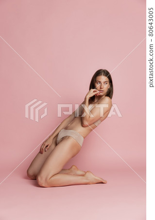 Portrait of young beautiful tanned woman in lingerie posing isolated over pink studio background. Natural beauty concept. Portrait of young beautiful tanned woman in lingerie posing isolated over pink studio background. Natural beauty concept. 80643005