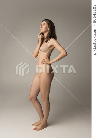 Portrait of young beautiful slim woman in lingerie posing isolated over gray studio background. Natural beauty concept. Portrait of young beautiful slim woman in lingerie posing isolated over gray studio background. Natural beauty concept. 80643105