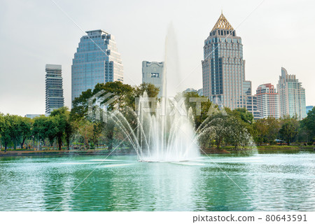 Lumphini park with lake, fountain and skyscrapers on skyline in Bangkok, Thailand Lumphini park with lake, fountain and skyscrapers on skyline in Bangkok, Thailand 80643591